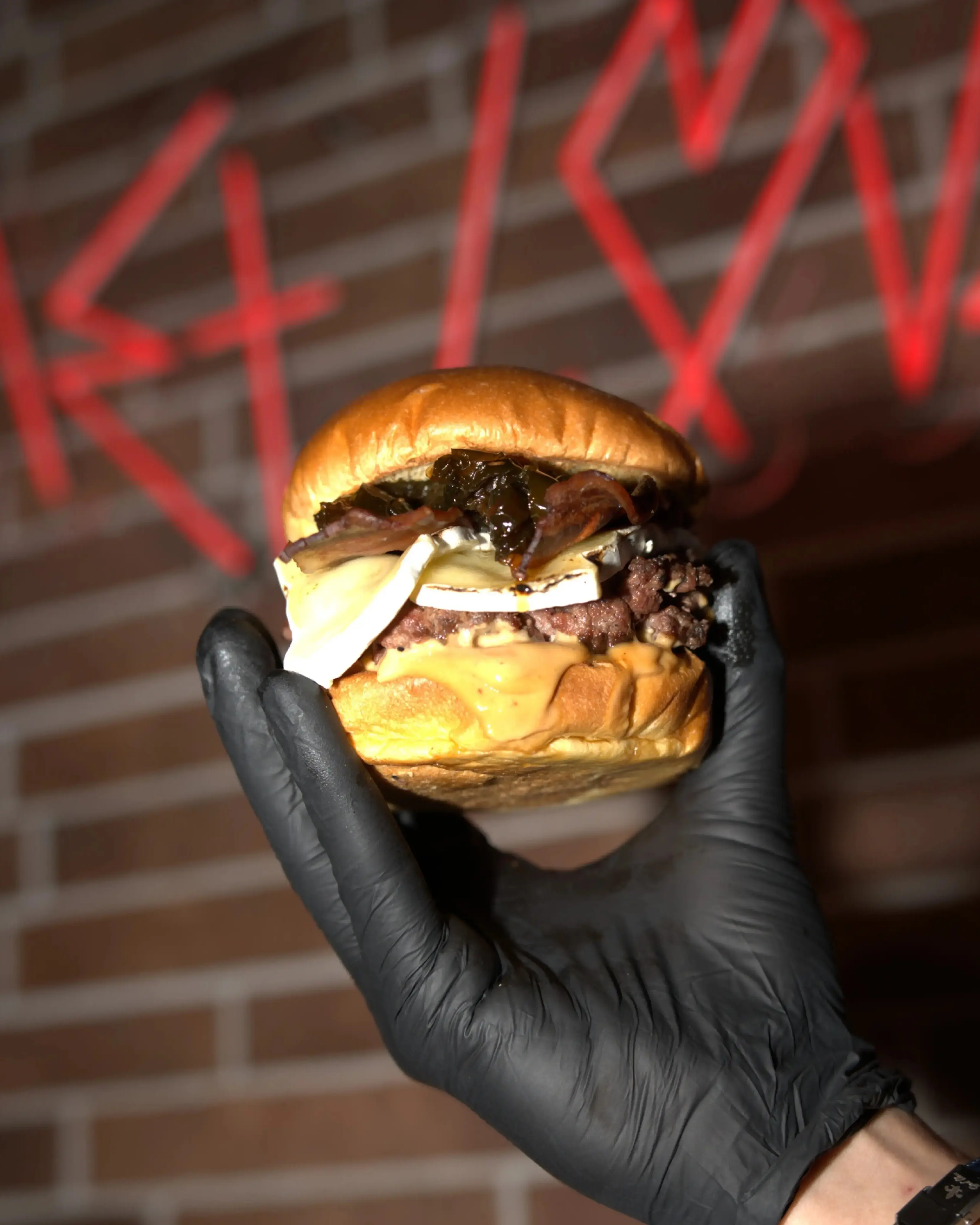 Burger del Mes de BURMET sostenida frente al neón del restaurante